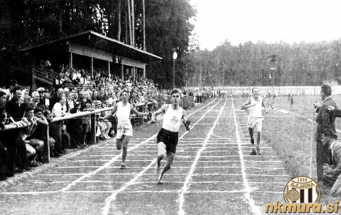 Pogled iz južnega dela stadiona proti severu med atletskim tekmovanjem ob otvoritvi stadiona; na levi strani je lesena tribuna, v ozadju za igriščem preko potoka Ledava pa gozd, ki se je takrat raztezal vse do prvih vasi Černelavci in Polana. Na fotografiji je atletsko tekmovanje ob otvoritvi stadiona. Aleksander Čisar je bos priboril prvo mesto.